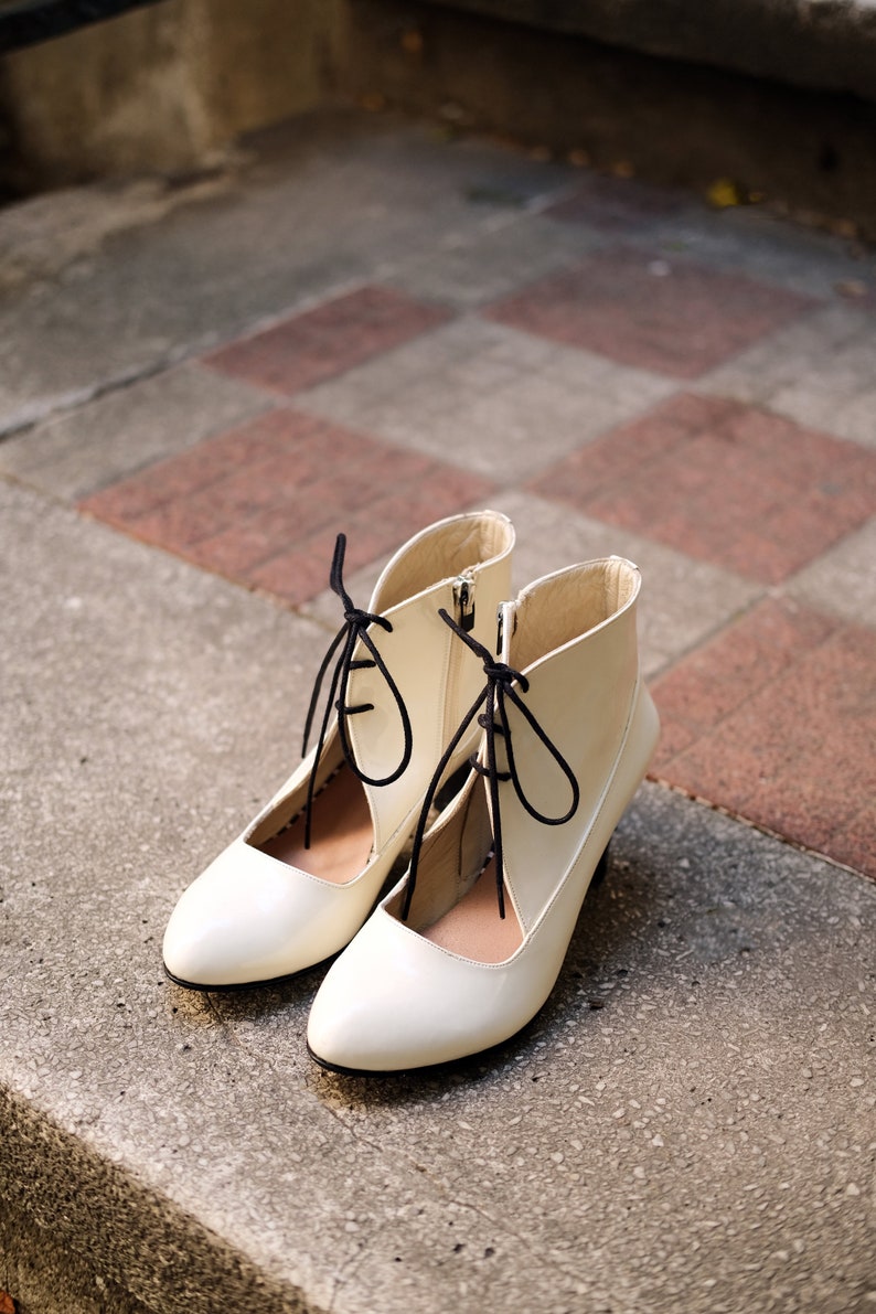 May include: A pair of white ankle boots with black laces. The boots have a pointed toe and a low heel.