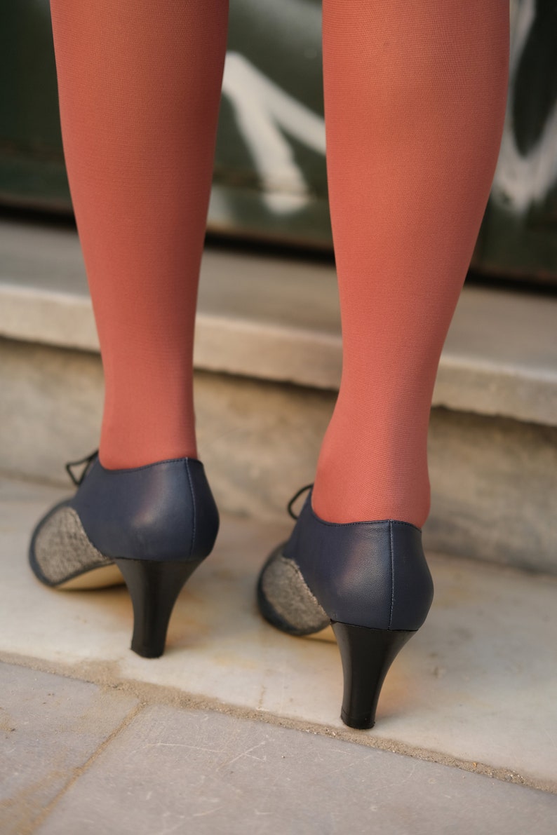 May include: A pair of navy blue heeled shoes with a tweed pattern on the toe. The shoes have a black heel and are worn with coral coloured tights.
