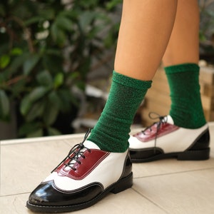 May include: White and black leather oxford shoes with a red accent on the side. The shoes are worn with green sparkly socks.