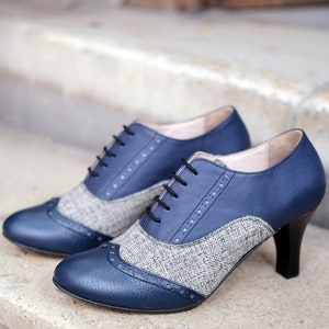 May include: A pair of blue and grey heeled shoes with a tweed pattern. The shoes have a lace-up front and a pointed toe.