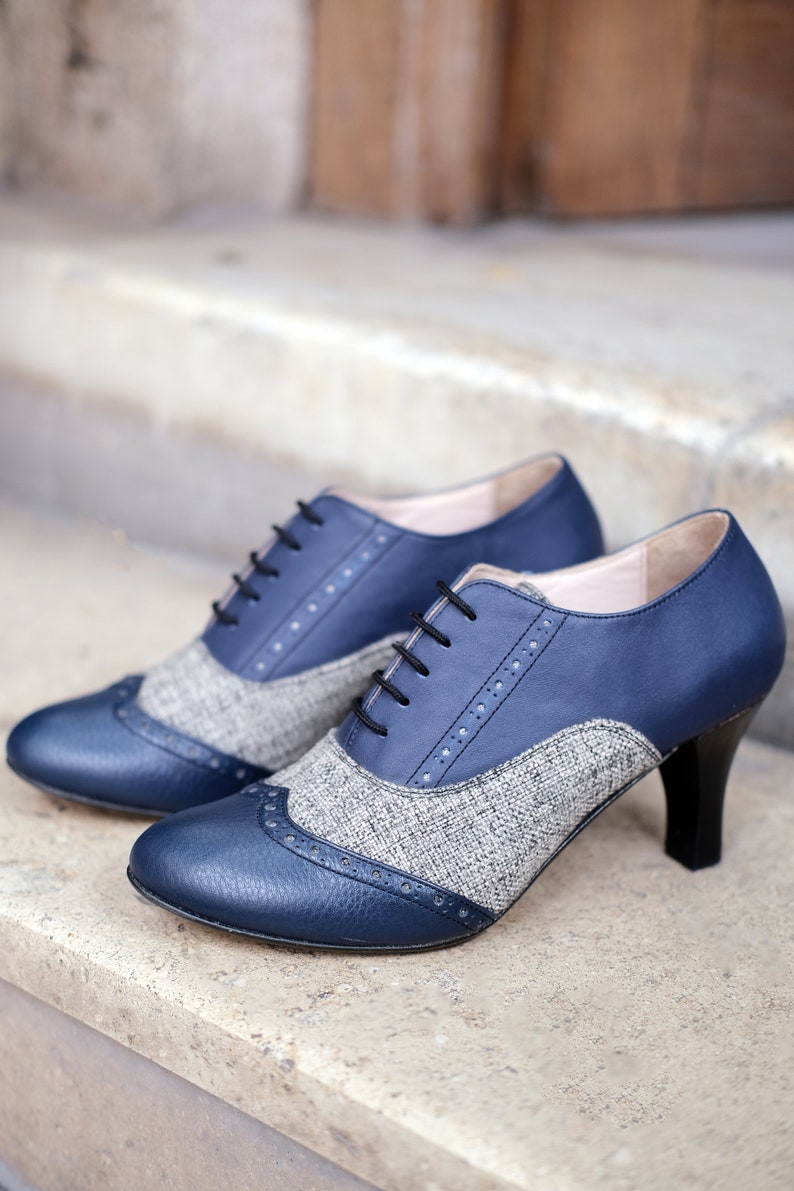 May include: A pair of blue and grey heeled shoes with a tweed pattern. The shoes have a lace-up front and a pointed toe.