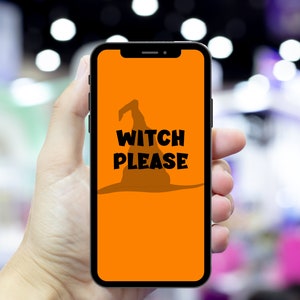 May include: A smartphone displays an orange screen with a black witch hat silhouette and the words "WITCH PLEASE" in bold black letters. The phone is held in a hand against a blurred background.