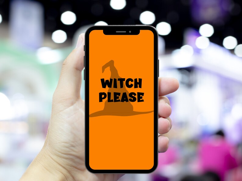May include: A smartphone displays an orange screen with a black witch hat silhouette and the words "WITCH PLEASE" in bold black letters. The phone is held in a hand against a blurred background.