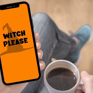 May include: A smartphone displays an orange screen with a witch hat silhouette and the words "WITCH PLEASE" in black. The phone is held in a hand, with a cup of coffee in the other hand. The theme is Halloween.