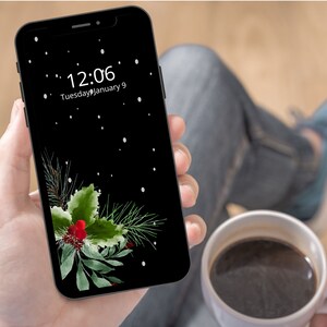 May include: A black smartphone with a dark green and red holly sprig design on the screen. The time is 12:06 and the date is Tuesday, January 9.