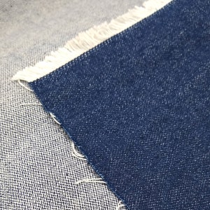 May include: Close-up of two different types of denim fabric. One is a light blue denim with a white fringe, and the other is a dark blue denim.