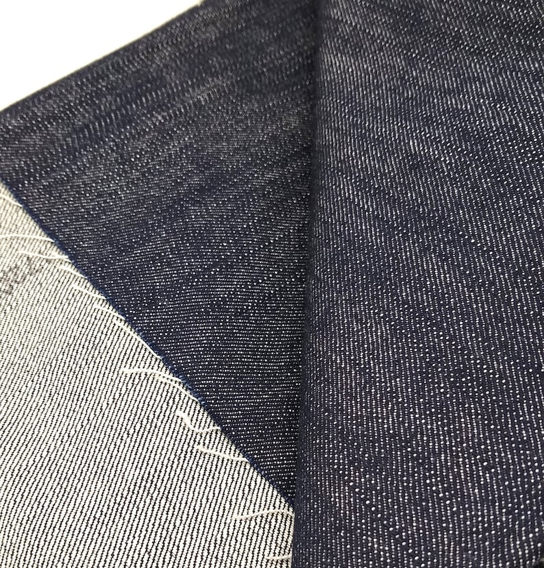May include: Close-up of two pieces of dark blue denim fabric. The fabric has a textured weave and a slightly faded appearance.