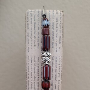 Puede incluir: Un marcapáginas de cuentas rojas y blancas con un dije de búho plateado. El marcapáginas tiene el texto "thanks for all you do".