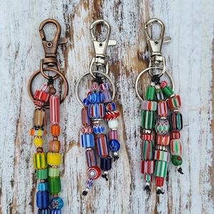 Puede incluir: Tres llaveros de cuentas coloridas con cierres plateados y de cobre. Cada llavero presenta una variedad de cuentas de vidrio en rojo, verde, azul y amarillo.