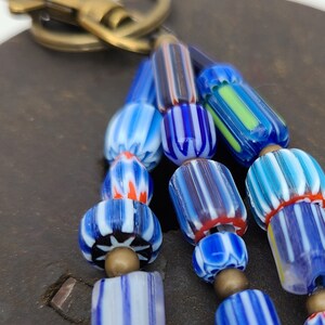 Puede incluir: Un llavero con un racimo de cuentas de vidrio de colores. Las cuentas est&aacute;n rayadas con azul, blanco y rojo, y algunas tienen un patr&oacute;n floral. El llavero est&aacute; unido a un anillo de lat&oacute;n.