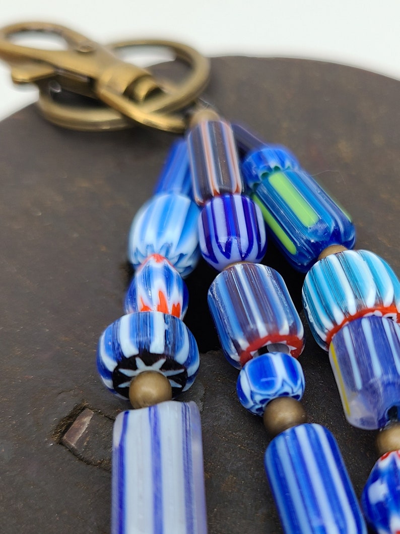 Puede incluir: Un llavero con un racimo de cuentas de vidrio de colores. Las cuentas est&aacute;n rayadas con azul, blanco y rojo, y algunas tienen un patr&oacute;n floral. El llavero est&aacute; unido a un anillo de lat&oacute;n.