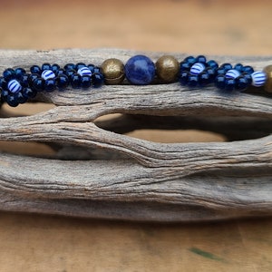 Puede incluir: Primer plano de un brazalete de cuentas azules y doradas con una piedra de lapislázuli. El brazalete está hecho con cuentas pequeñas y redondas y tiene un diseño floral.