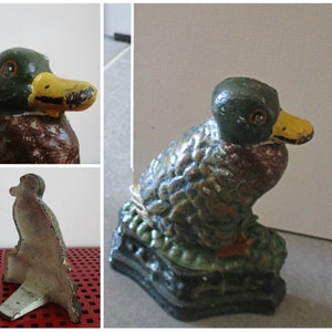 May include: A cast iron duck doorstop with a green, brown, and yellow paint finish. The duck is sitting on a base with a green and brown leafy design.