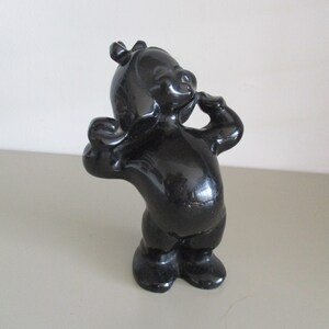 May include: A black ceramic figurine of a cartoon character with a crown on its head, standing with its arms raised and a hand on its chin.