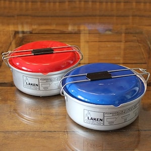May include: Two round aluminum food containers with lids. The container on the left has a red lid and the container on the right has a blue lid. Both containers have a silver base with the word "LAKEN" printed on them.