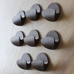 May include: Eight dark brown wooden hooks mounted on a light brown wall. The hooks are shaped like a crescent moon with a small lip on the inside.