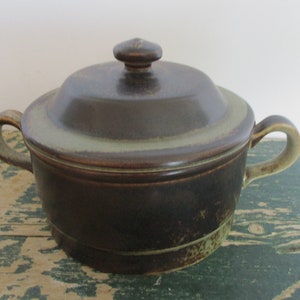 May include: A brown ceramic casserole dish with a lid. The dish has a green glaze and a brown rim. The lid has a knob on top.