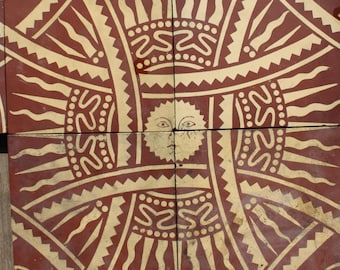 May include: A set of terracotta-coloured tiles featuring a repeating sun design. The sun has a face at the centre, encircled by radiating lines and decorative patterns in cream. The tiles are arranged together, displaying the complete design.