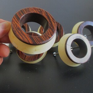 May include: A set of five wooden rings with a light brown and dark brown striped pattern. The rings are stacked on top of each other and have a white inner ring.