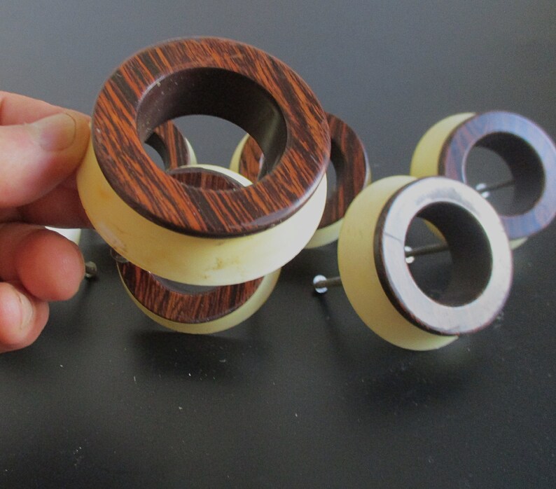 May include: A set of five wooden rings with a light brown and dark brown striped pattern. The rings are stacked on top of each other and have a white inner ring.
