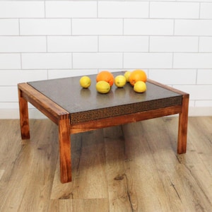 Pode incluir: Uma mesa de centro de madeira castanho escura com tampo de vime. A mesa está sobre um piso de madeira castanho claro. Há várias laranjas e limões sobre a mesa.