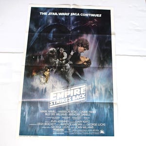 May include: A vintage movie poster for "Star Wars: The Empire Strikes Back." The poster features a dramatic scene with characters and the text "THE STAR WARS SAGA CONTINUES." The poster has a blue and white color scheme.