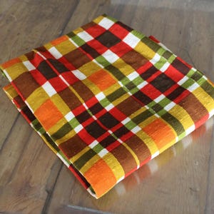 May include: Folded square fabric with a plaid pattern in shades of orange, red, brown, yellow, green, and white. The fabric is likely a tablecloth or a similar textile item.