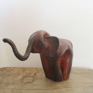 May include: A wooden elephant sculpture with a curved trunk and large ears. The elephant is a rich brown colour and appears to be carved from a single piece of wood. The sculpture is displayed on a wooden surface.