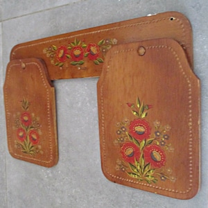 May include: Three wooden wall decor pieces with hand-painted floral designs in red, yellow, and green. The pieces are connected and have a rustic, vintage look.