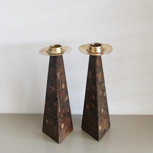 Pode incluir: Um par de castiçais de madeira com topos de latão. Os castiçais têm a forma de uma pirâmide e apresentam um padrão geométrico.