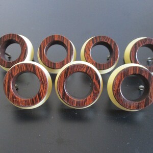 May include: Set of seven wooden drawer pulls with a brown and cream color scheme. The pulls are round with a hole in the center for a screw.