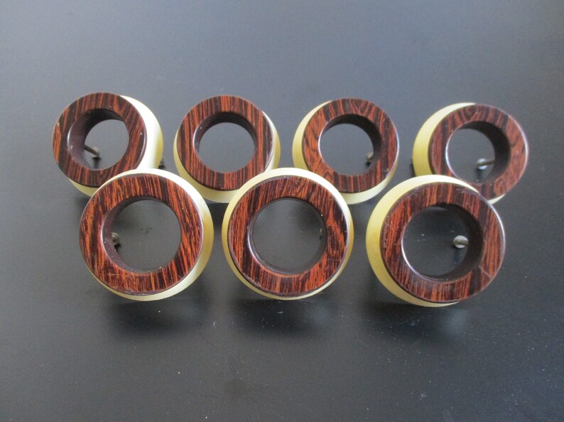 May include: Set of seven wooden drawer pulls with a brown and cream color scheme. The pulls are round with a hole in the center for a screw.