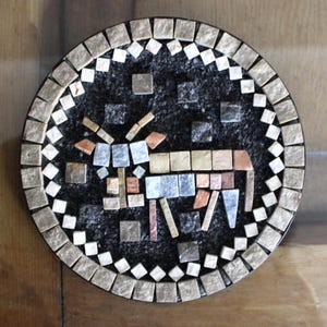 Pode incluir: Obra de arte em mosaico redondo com uma figura de animal estilizada. A obra de arte tem um fundo preto com uma borda de azulejos quadrados em tons neutros. O animal é composto por azulejos de várias cores, incluindo prata, cobre e bege.