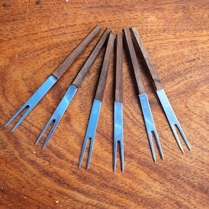 Può includere: Set di sei forchette da portata con rebbi in acciaio inossidabile e manici in legno scuro. Le forchette sono disposte su una superficie di legno, ideali per antipasti o piccoli assaggi.