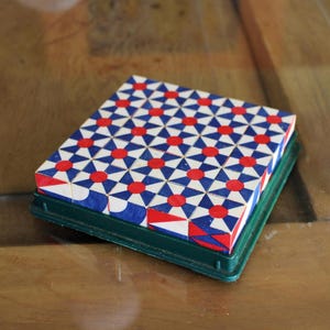 Peut inclure: Un puzzle carré avec un motif géométrique de cercles rouges et de formes bleues et blanches. Le puzzle est dans un plateau en plastique vert, posé sur une surface en bois. Le motif est répété sur toute la surface du puzzle.