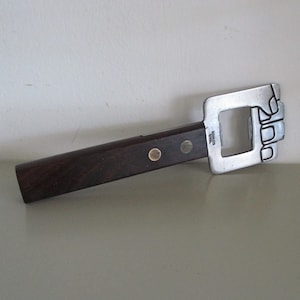 May include: A silver bottle opener with a wooden handle. The opener is shaped like a fist and has the words "Stainless Steel" engraved on it.