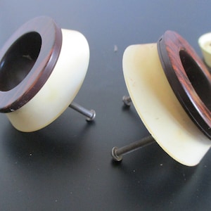 May include: Three vintage cabinet knobs with a brown wood grain design and a white plastic base. Each knob has a screw for attaching to a cabinet door.