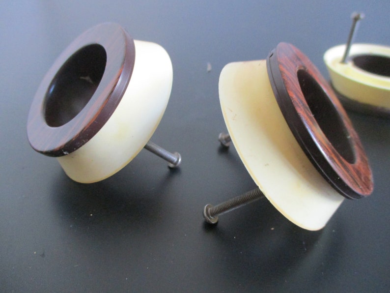 May include: Three vintage cabinet knobs with a brown wood grain design and a white plastic base. Each knob has a screw for attaching to a cabinet door.