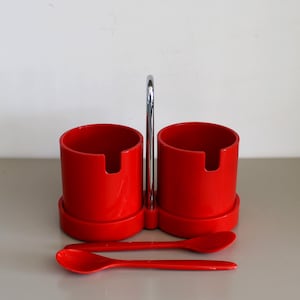 Könnte beinhalten: Ein rotes Keramik-Zucker- und Sahne-Set mit einem verchromten Griff und zwei roten Löffeln.