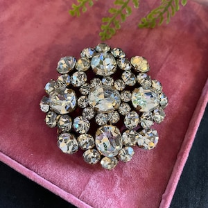 May include: A large, round, clear crystal brooch with a gold tone setting. The brooch is made up of many individual crystals of varying sizes, all set in a circular pattern.