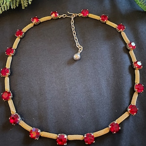 May include: A gold chain necklace with red gemstone accents. The chain is made of a fine mesh and the gemstones are round and faceted.