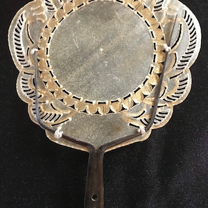 May include: A decorative fan with a round, silver-coloured, cutout design. The fan has a black wooden handle with three holes.