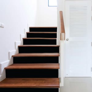 May include: A wooden staircase with black risers and a white wall. The steps are made of light brown wood, and the risers are painted black. A white door with horizontal slats is visible.