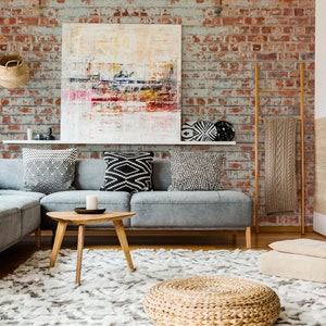 May include: A living room with a gray sectional sofa, a coffee table, and a fireplace. The room is decorated in a bohemian style with a variety of throw pillows, blankets, and woven baskets. The wall behind the sofa is covered in a brick wallpaper.
