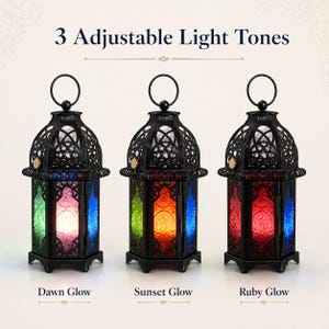 May include: Three black metal lanterns with intricate cut-out patterns and hanging rings. Each lantern displays different colored glass panels and internal light settings labeled as Dawn Glow, Sunset Glow, and Ruby Glow. Text reads 3 Adjustable Light Tones.