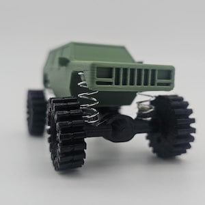 May include: A green toy truck with black wheels and a detailed front grill. The truck has a suspension system with springs visible.