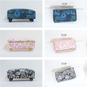 May include: A set of three decorative footstools with different patterned upholstery. One features a peacock feather design, another a pink leopard print, and the third a black and white zebra pattern. Each stool has small, rounded legs.