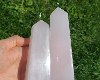 May include: Two selenite crystal points, one larger than the other, with a white, translucent, and slightly iridescent appearance. The crystals are displayed against a green grassy background.