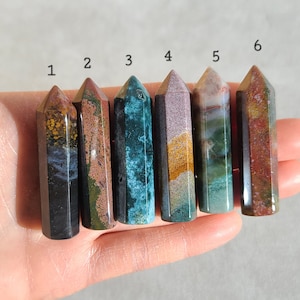 May include: Six polished gemstone points in various colors and patterns, including black, green, brown, and white. The points are arranged in a row from left to right, numbered 1 through 6.