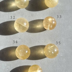 May include: Six yellow citrine crystal spheres, numbered 30 to 36, arranged in rows on a grey surface.